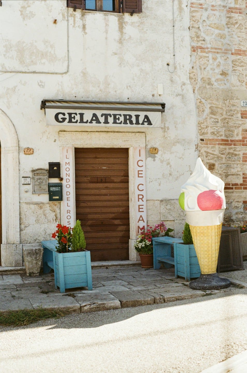 Ingresso di una gelateria con scultura di gelato e fioriere.