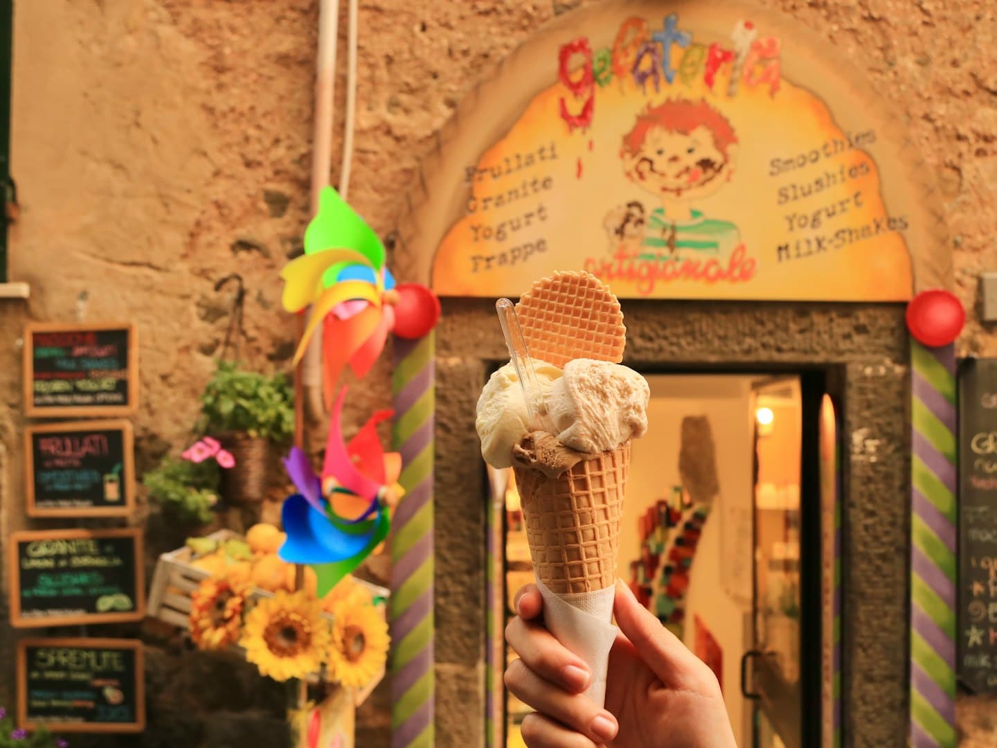 Mano che tiene un cono waffle con tre palline di gelato.
