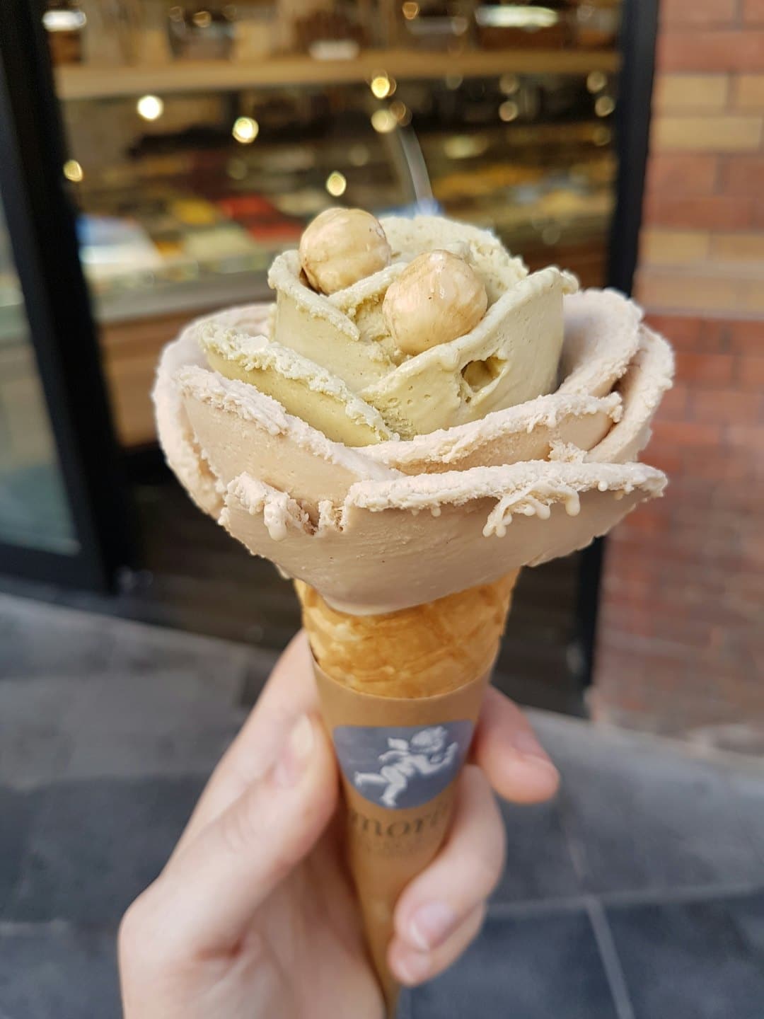 Mano che tiene un cono gelato a forma di rosa con nocciole.