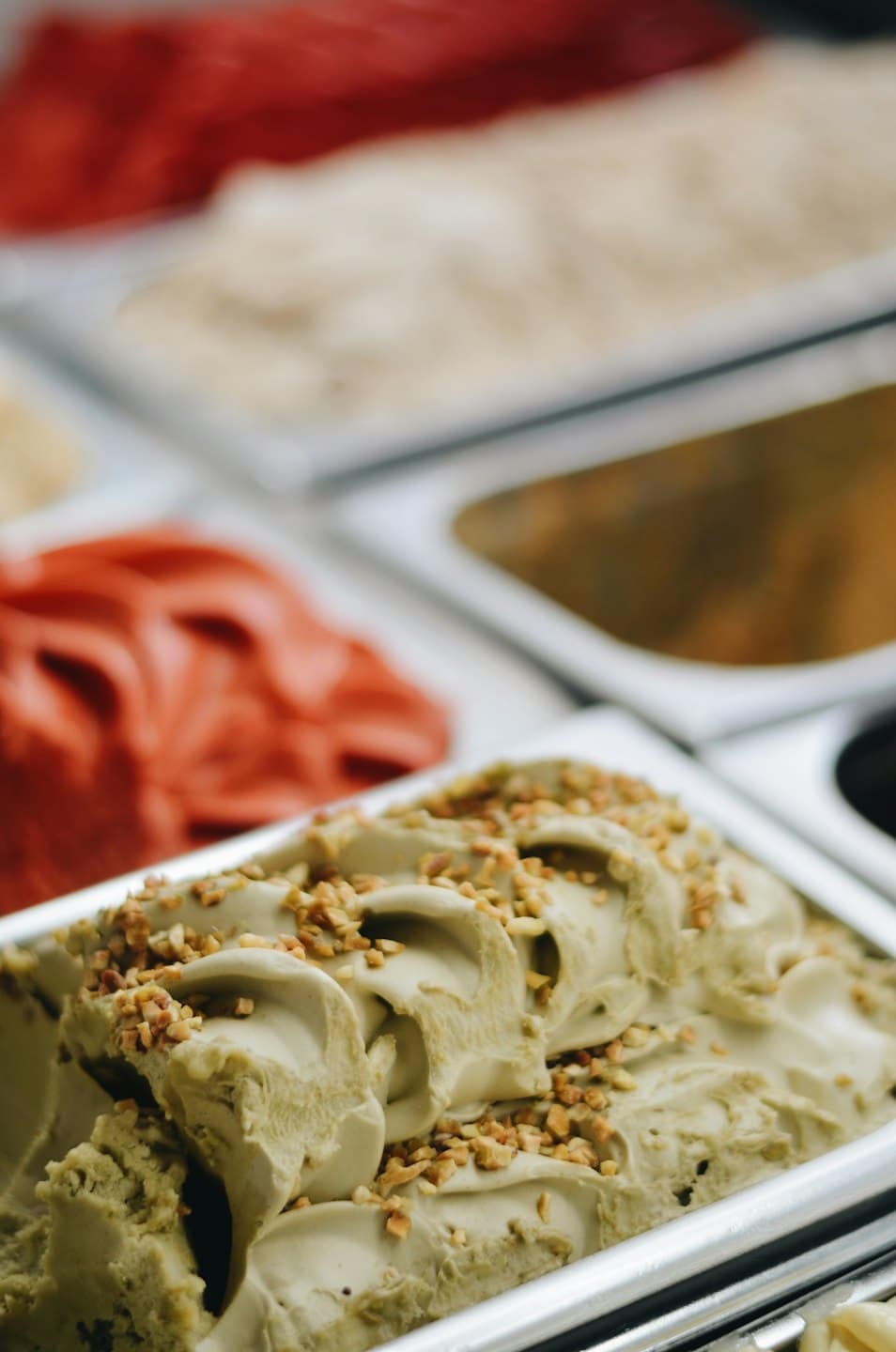 Gelato al pistacchio con granella di nocciole in vaschette di metallo.